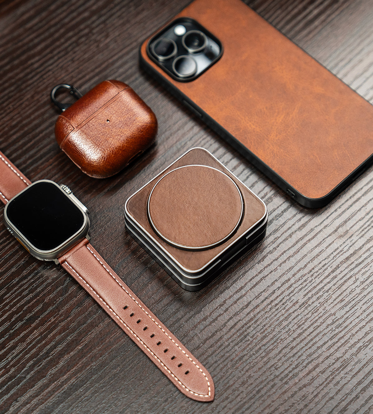 Brown leather phone case, watch strap, and square pouch on a wooden surface