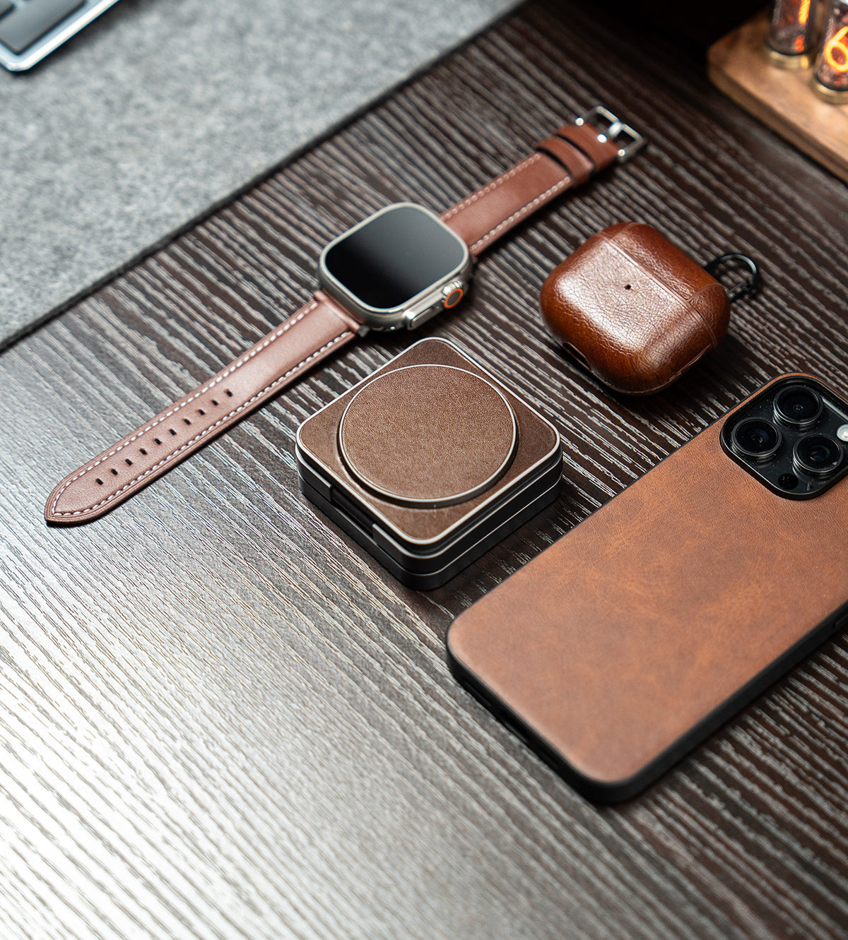 Brown leather accessories including a watch, phone case, and coasters on a wooden surface.